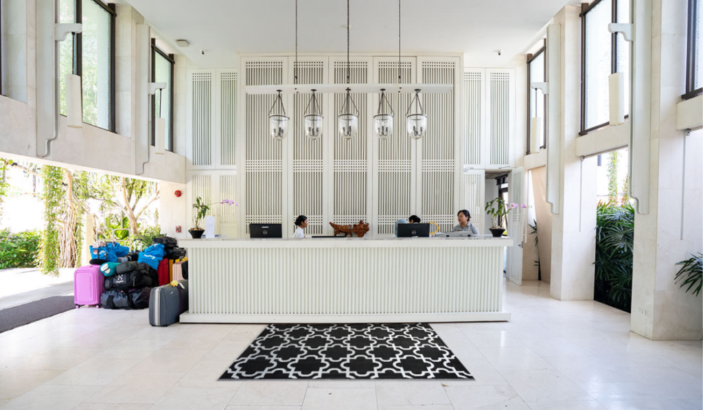 Białe pomieszczenie z recepcją umieszczoną na środku, obok znajdują się walizki