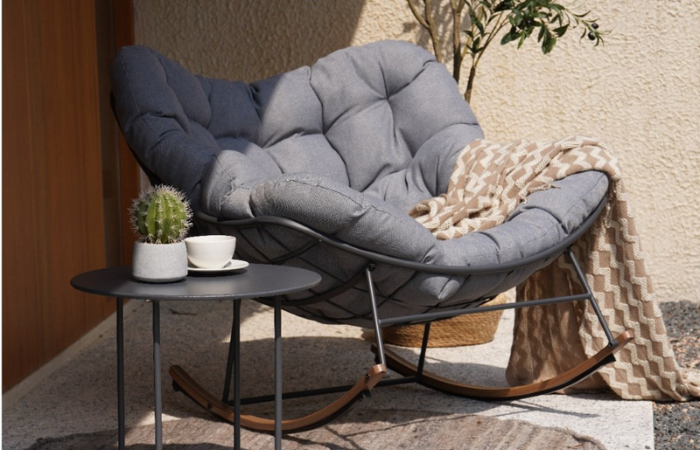 wodoodporne, wygodne, krzesło/fotel bujany ustawione na tarsie z kocem i stolikiem z kwiatami 