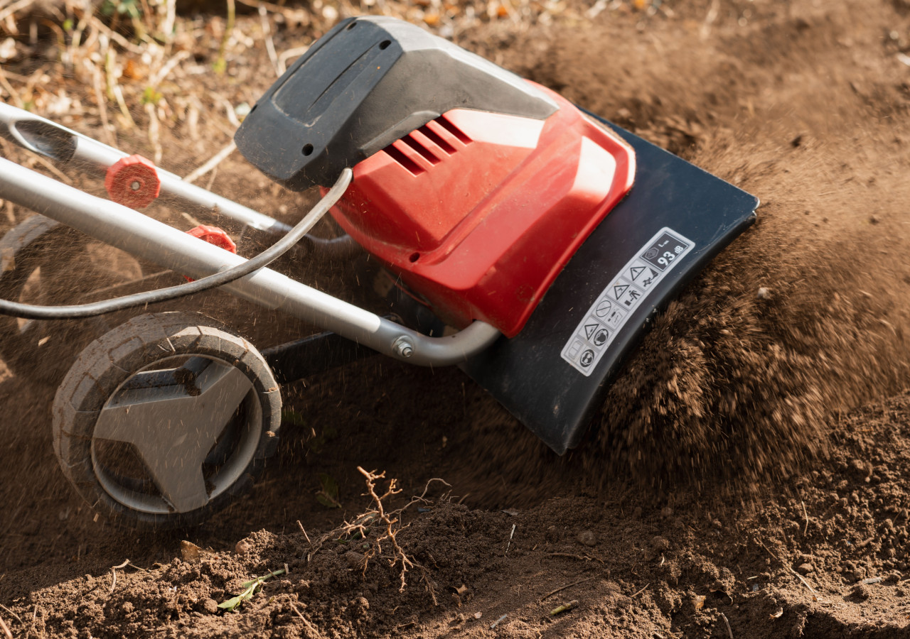 Glebogryzarka elektryczna z czerwono-czarną obudową spulchnia ziemię w ogrodzie