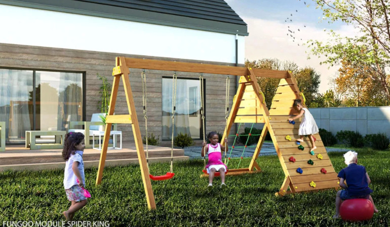 Dzieci bawiące się na placu zabaw, kt&oacute;re stoi przed domem jednorodzinnym