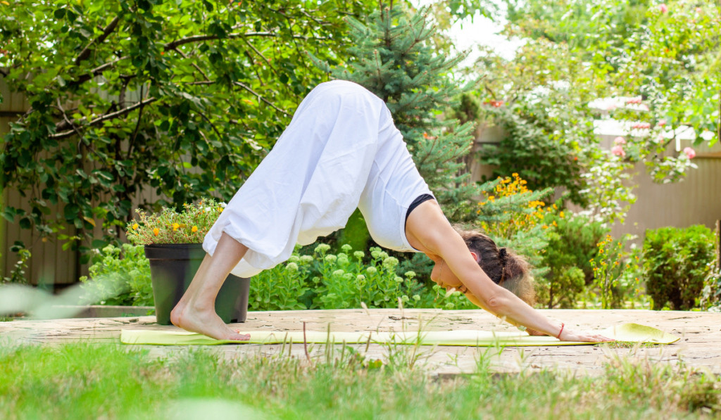 Kobieta w białym stroju uprawiająca Jogę w ogrodzie pośr&oacute;d zielonych roślin
