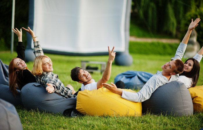 grupa przyjaci&oacute;ł spędzająca czas w ogrodzie na bean bagach na kinie plenerowym