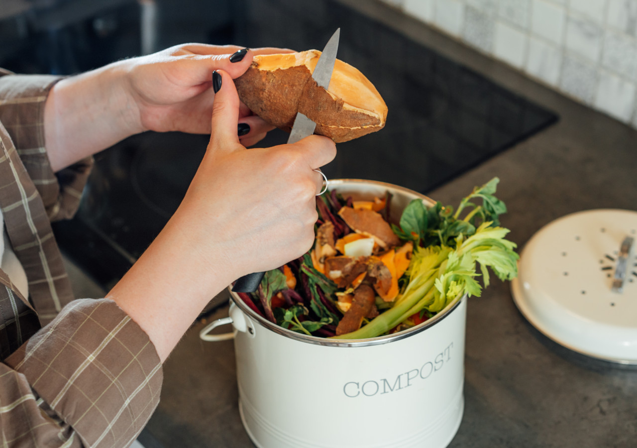 Kobieta obiera warzywa do wiaderka z napisem kompostownik