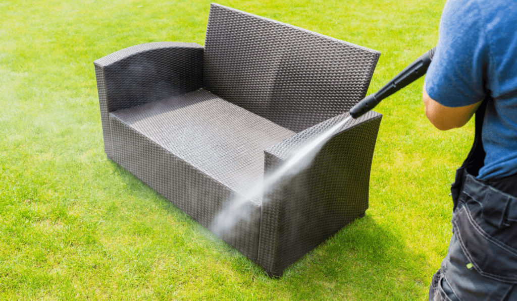 Mężczyzna czyści mebel wodą z węża na podw&oacute;rku 