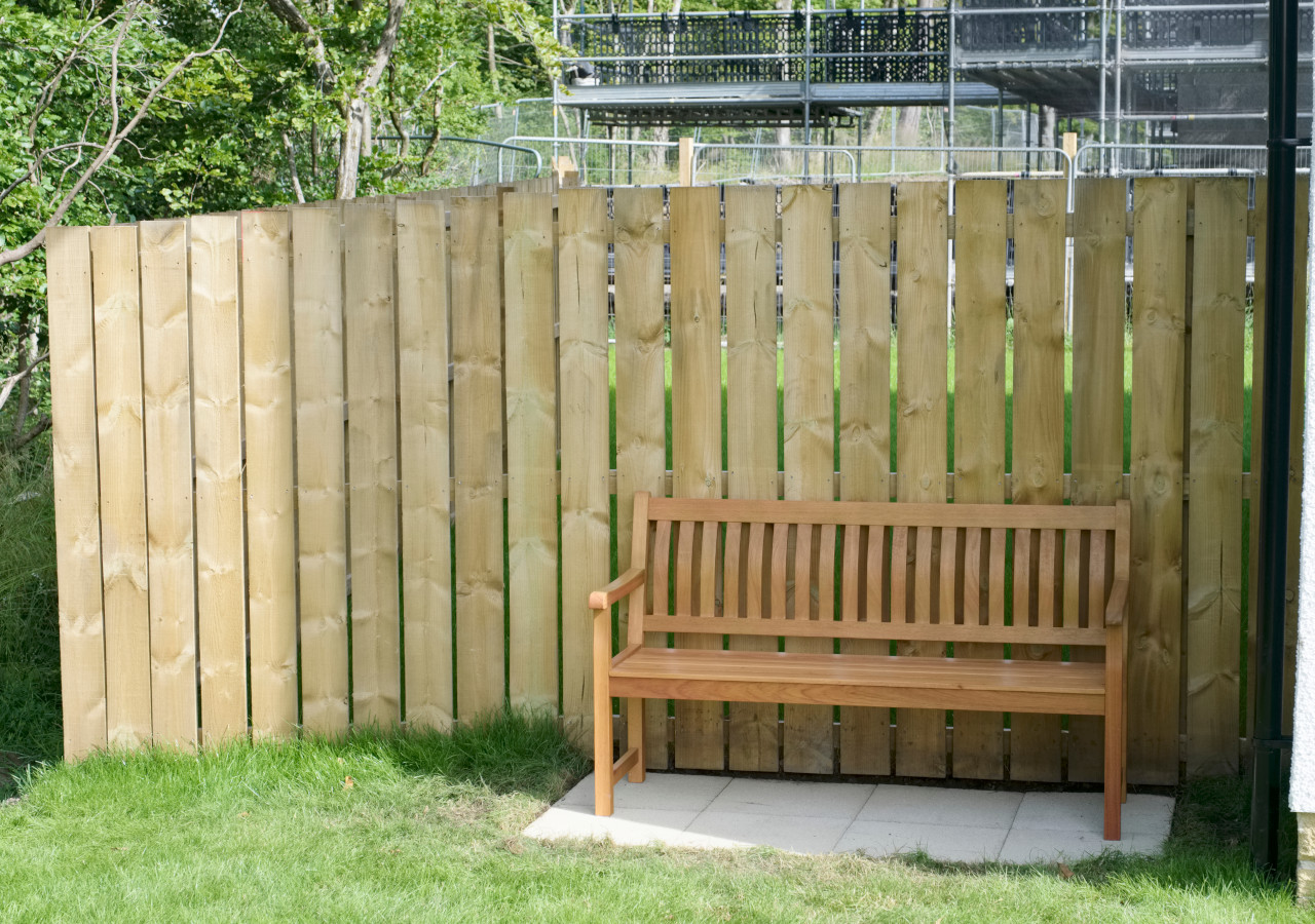 Ławka ustawiona pod drewnianym płotem