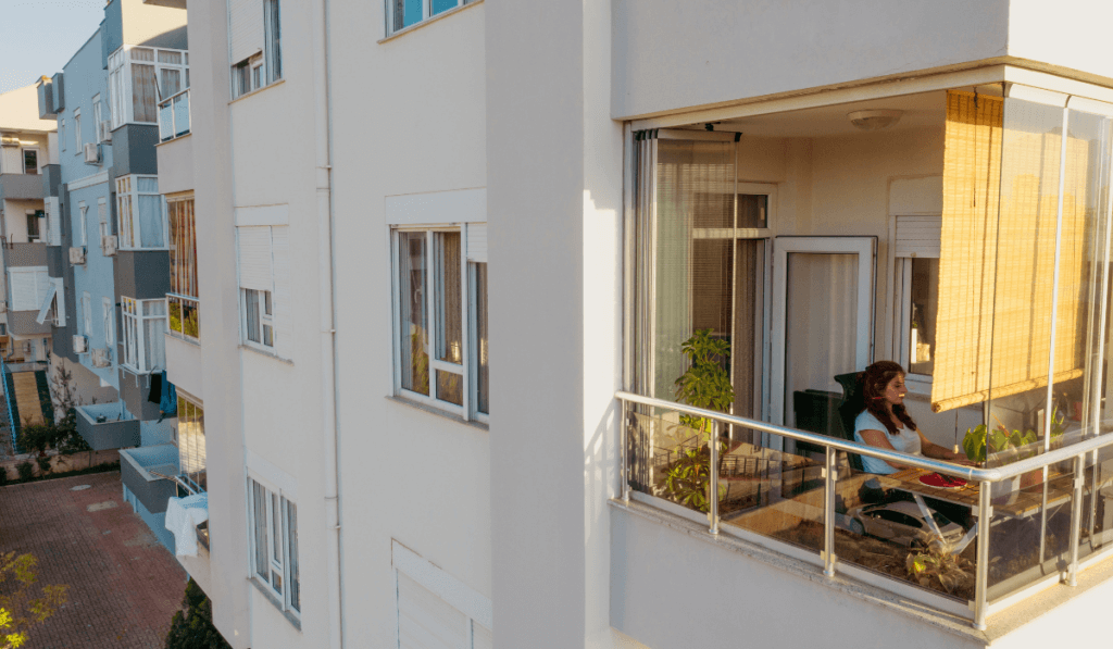 Widok na balkon bloku mieszkalnego na kt&oacute;rym siedzi kobieta