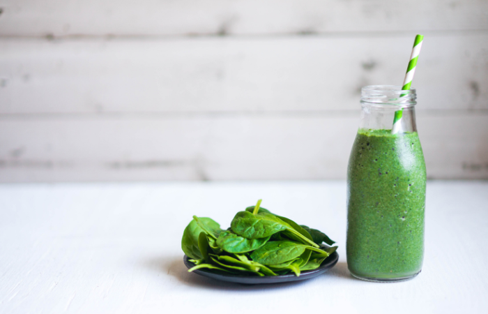 liście szpinaku na talerzu a obok butelka ze szpinkowym Smoothie