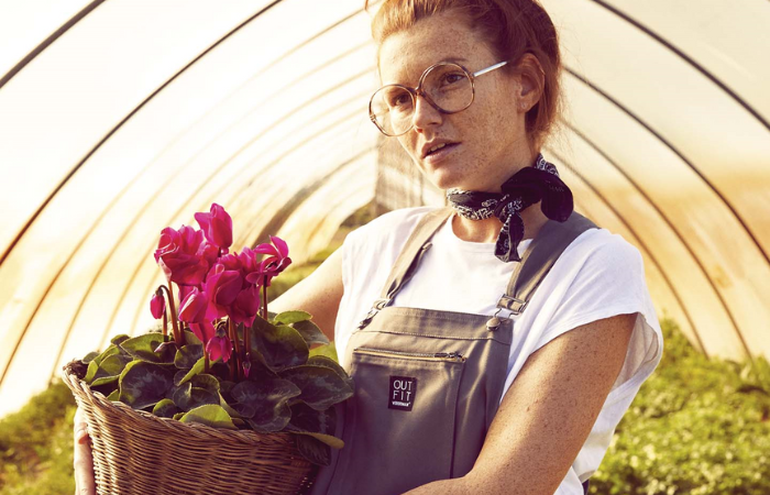 kobieta w ogrodniczkach trzymająca rośliny w doniczce w tunelu ogrodowym