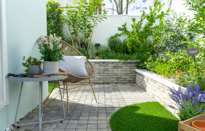 niewielki ogrd&oacute; w mieście gesto obsadzony kwiatami i ziołami z krzesłem i stolikiem 