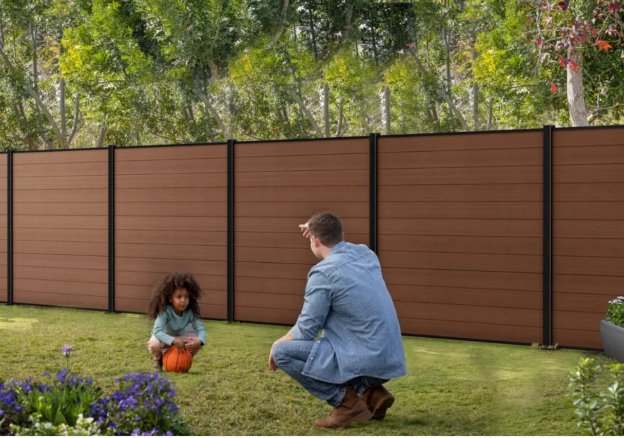 Ojciec i c&oacute;rka kucają w ogrodzie przed brązowym płotem
