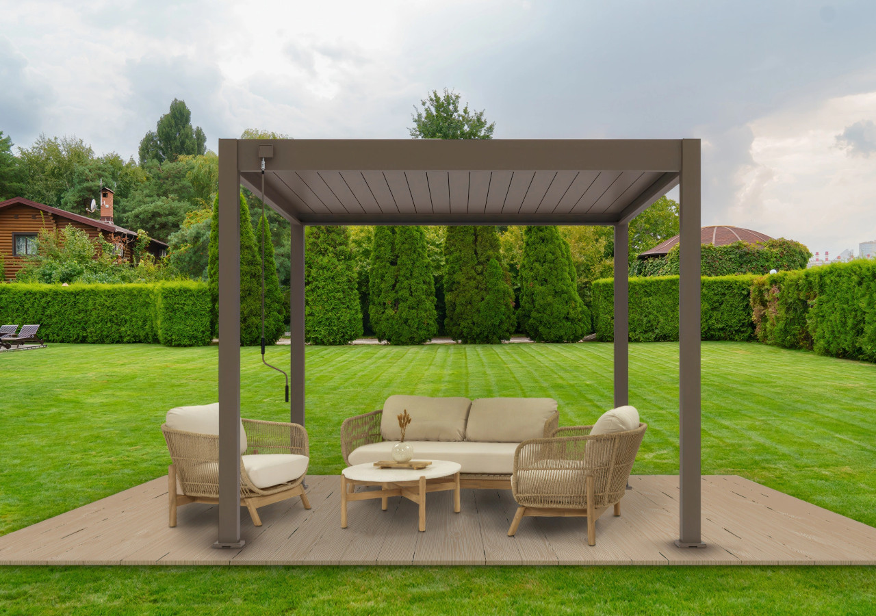 Beżowa pergola ogrodowa z zestawem rattanowych mebli wypoczynkowych na drewnianym podestie, ustawiona na tle zadbanego trawnika i wysokich żywopłotów