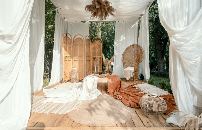 Altanka ogrodowa z rustykalną beżową dekoracją na piknik w ogrodzie, projekt zewnętrzny. Meble wiklinowe na zewnątrz w pergoli boho, nowoczesne podw&oacute;rko domowe. Letnia altana z naturalną rośliną, drewnianym wystrojem i kocami.