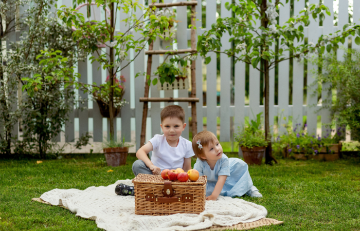 Młodszy brat i siostra urządzili piknik na podw&oacute;rzu domu w ogrodzie. Słodkie dzieci bawiące się razem.