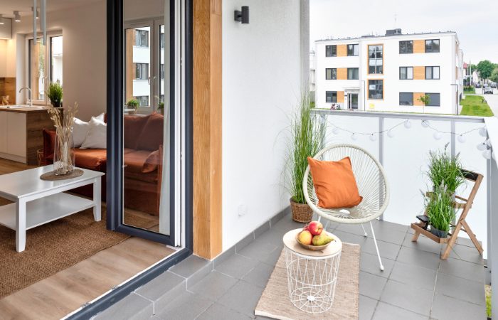 balkon w bloku wylożony szarymi płytkami z mały stolikiem balkonowym i fotelem  i kwietniczkiem z ziołami 