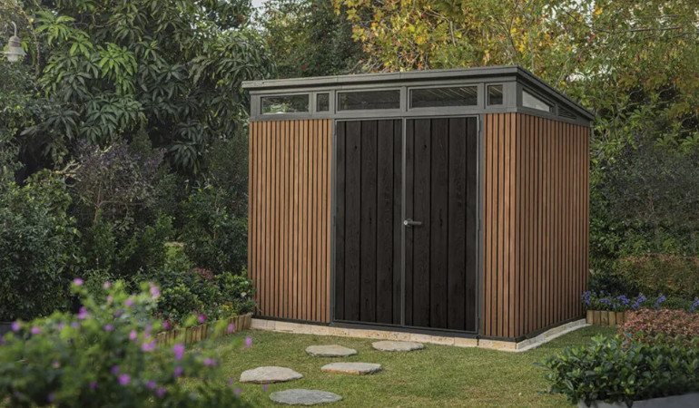 Domek narzędziowy PENTHOUSE 9x7 Brown Signature Collection - Keter w ogrodzie okalany zielenią wkiatami i drzewami