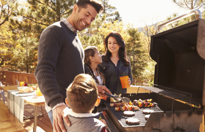 uśmiechnięta rodzina szykująca posiłki na grillu ogrodowym 