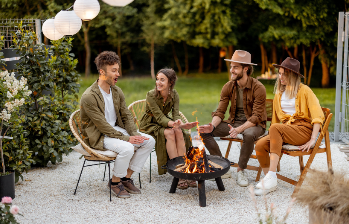 grupa przyjaci&oacute;ł spędzająca czas w ogrodzie przy palenisku ogrodowym 