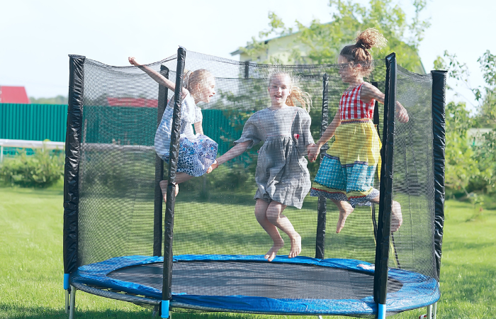 troje dzieci skaczących na trampolinie ogrodowej w słoneczny letni dzień 