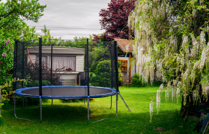 trampolina ogrodowa ustawiona w działce z domkiem letniskowym