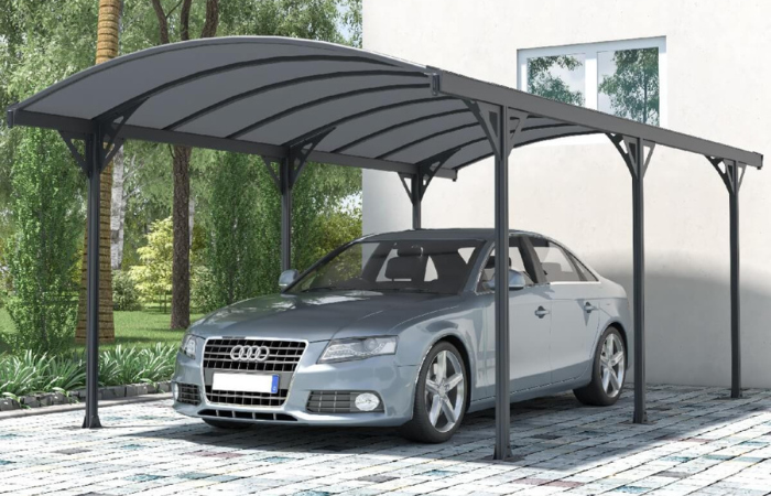 aluminiowa wiata garażowa ustawiona przed domem na kostce brukowej a pod nią wstawiony srebrny samoch&oacute;d audi 