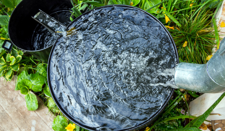 Woda przelewająca się z rynny do czarnego pojemnika 