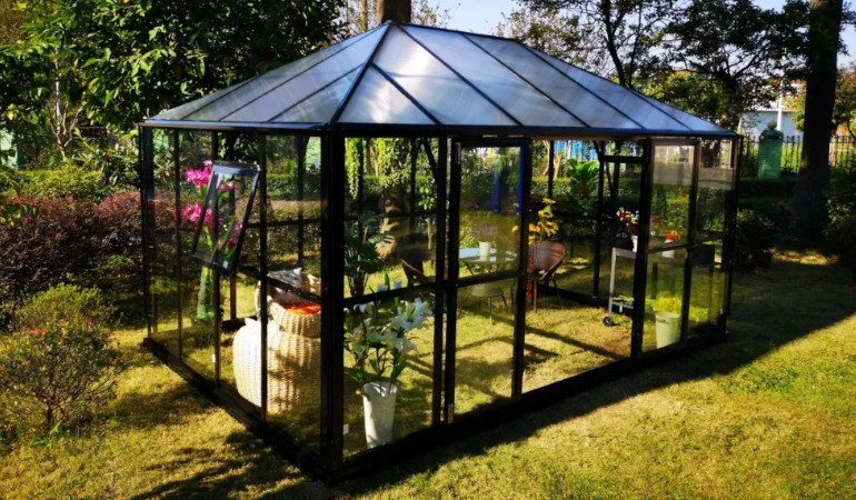 Oranżeria ogrodowa BROADWAY BLACK od Gutroof w otoczeniu zieleni, wyposarzona w meble ogrodowe oraz rośliny